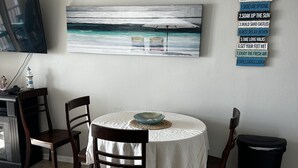 Un coin repas avec une table ronde, des chaises, un tableau et un panneau indiquant les règles à respecter dans la maison de vacances.