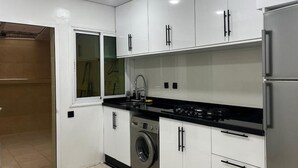 Een moderne keuken met witte kasten, een roestvrijstalen koelkast, een wasmachine en een zwart aanrecht.
