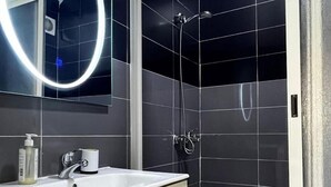 Een moderne badkamer met een wit wastafelmeubel, spiegel en donker betegelde wanden.