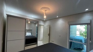 Een slaapkamer met een bed, een kledingkast, een deur naar een balkon en een plafondlamp.