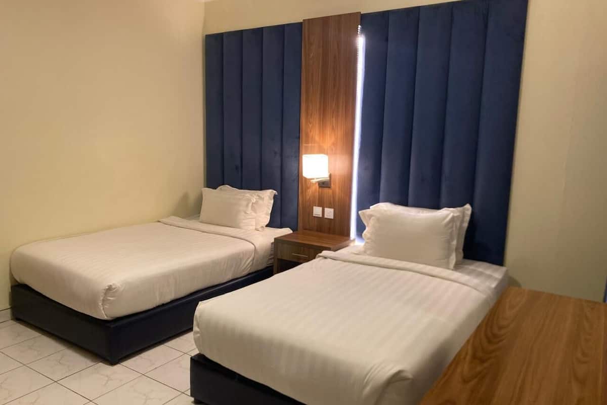 A hotel room with two single beds, a wooden nightstand, a wall-mounted lamp, and a large window with curtains.
