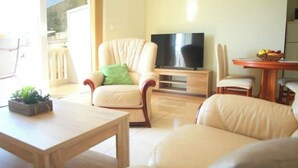 Ein Wohnzimmer mit Fernseher, einem Esstisch mit Stühlen und einer Topfpflanze.