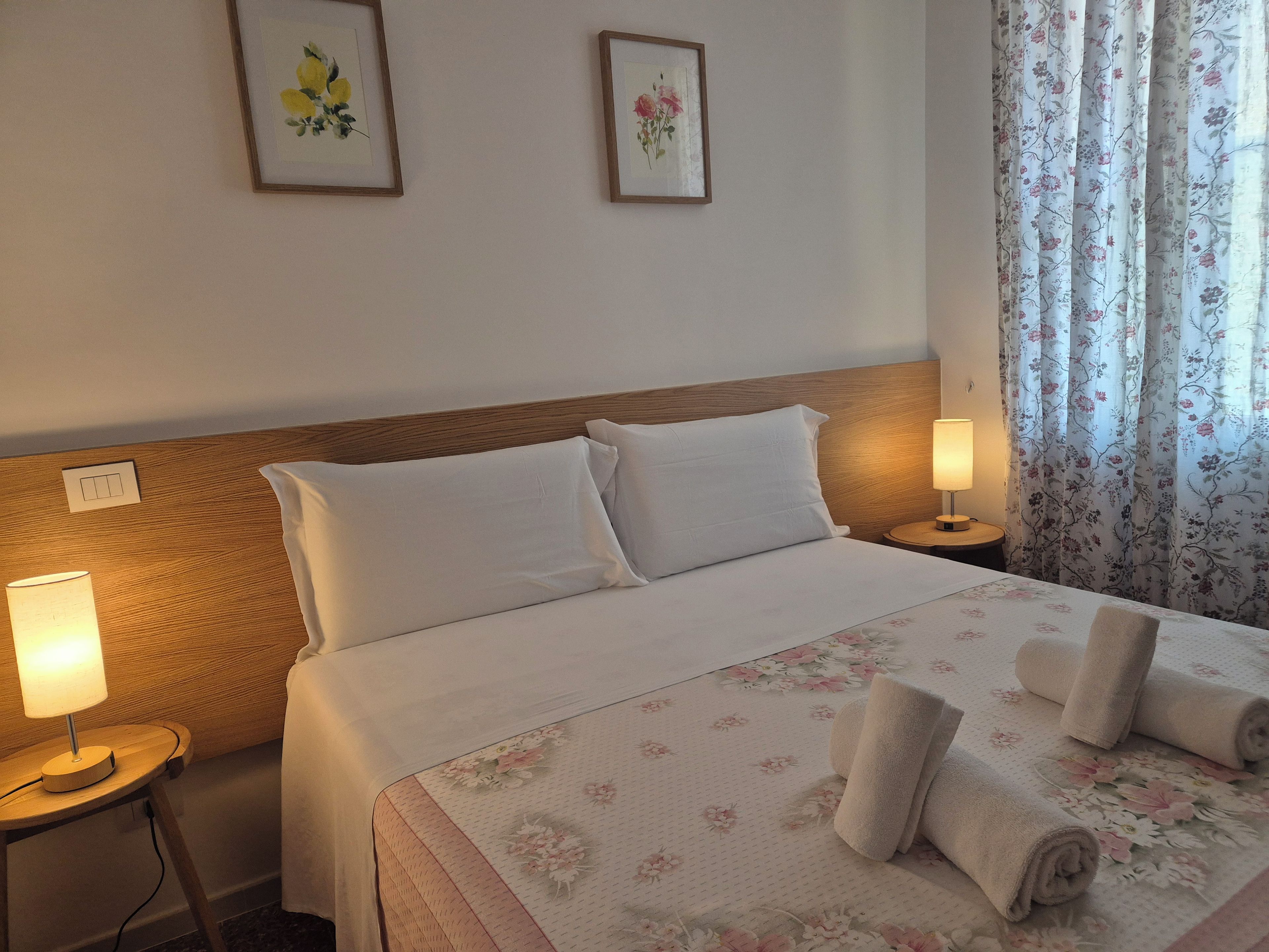 A hotel room with a bed, two bedside lamps, a night switch, and a floral bedspread.