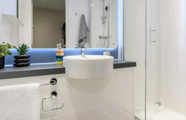 Une salle de bain moderne avec un lavabo blanc, une douche en verre et un mur d’accent bleu.