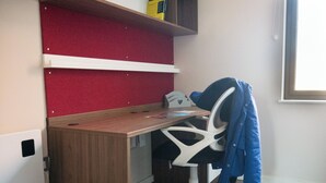 Un petit bureau avec un bureau en bois, une chaise de bureau blanche et un mur rouge.
