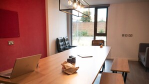 Une salle de conférence avec une longue table, deux ordinateurs portables, une tasse de café et un sac en papier. Il y a deux chaises et un banc.
