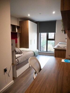 Quarto compacto com cama, escrivaninha e janela.
