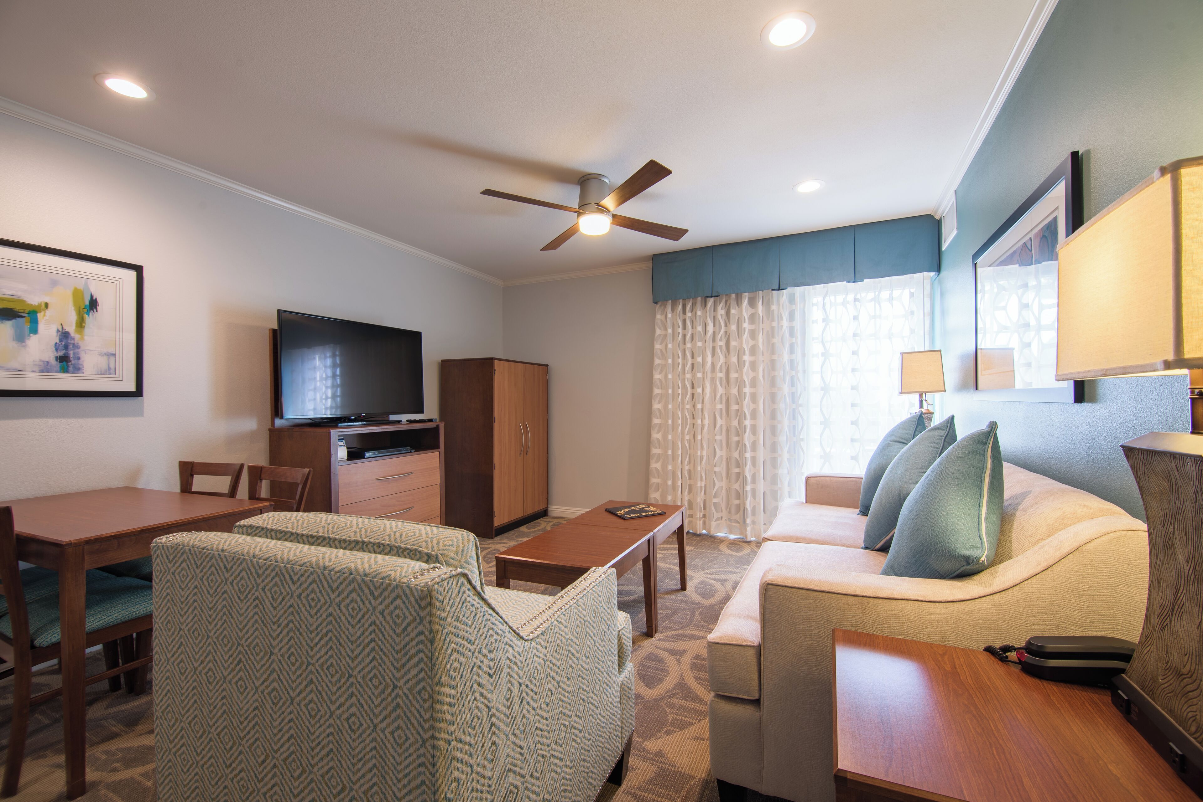 Habitación de hotel con comedor, sofá, televisor y ventilador de techo.