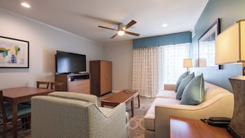 A hotel room with a dining area, a sofa, a television, and a ceiling fan.