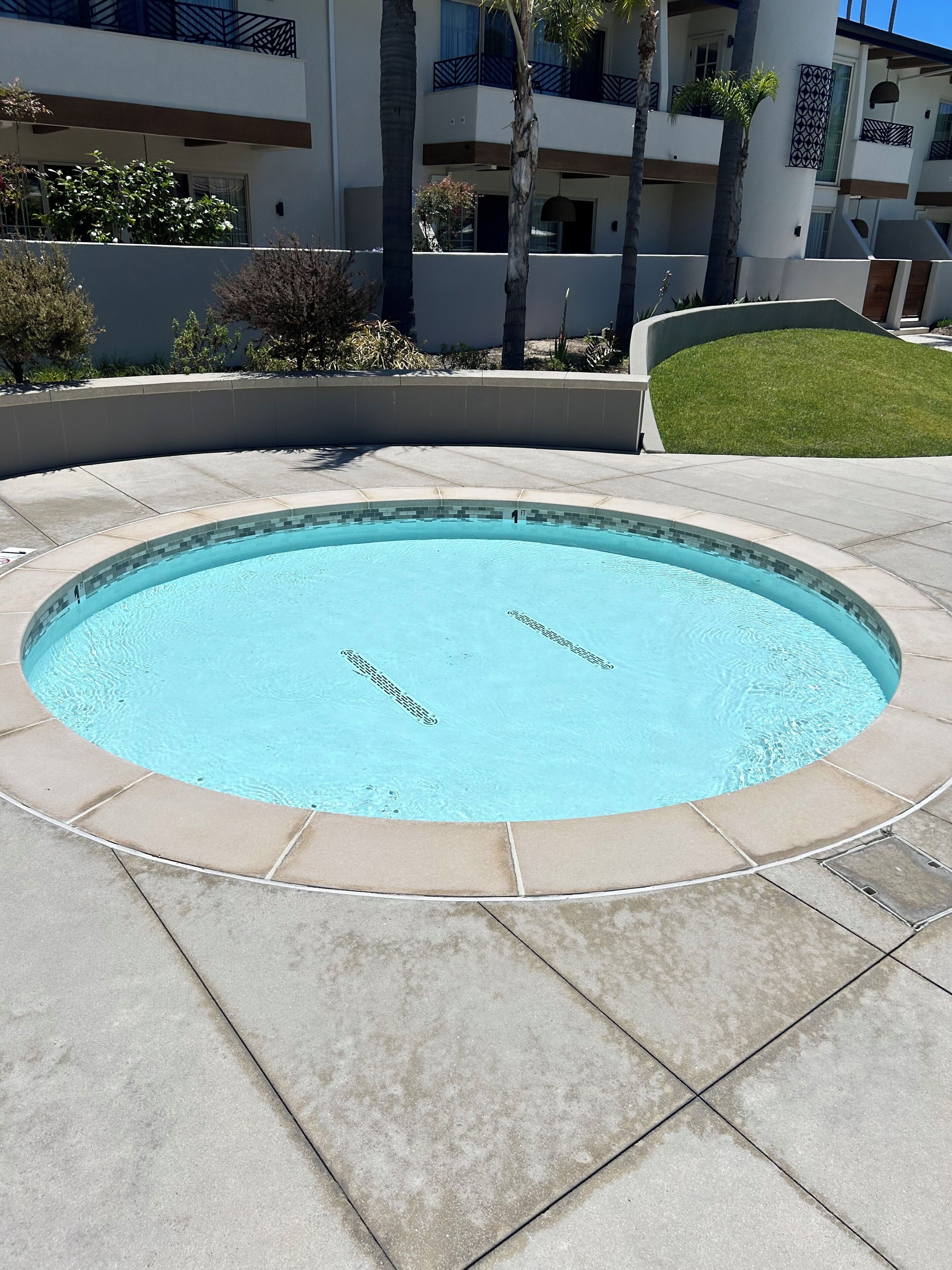 A swimming pool with a tiled edge, surrounded by a low wall and a grassy area.