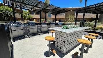 Un área de cocina exterior con una parrilla, taburetes de bar y una isla con diseño.