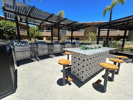 Un área de cocina exterior con una parrilla, taburetes de bar y una isla con diseño.