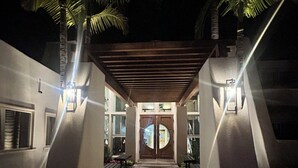 A nighttime view of a building entrance with a covered walkway, palm trees, and benches. - Winners Circle Solana Beach Del Mar Resort (Solana Beach)