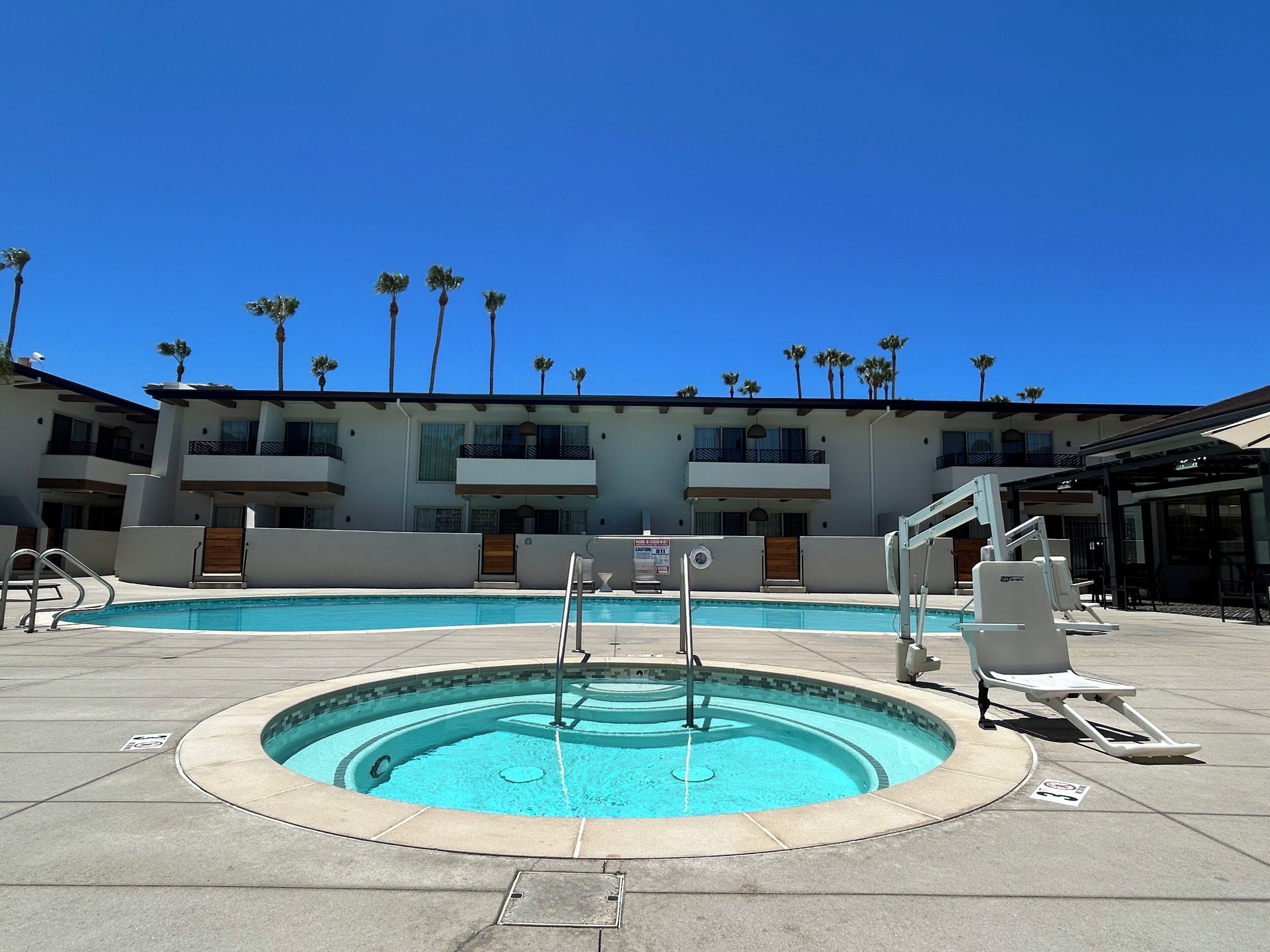 A swimming pool with a circular design, surrounded by a building with balconies and palm trees.