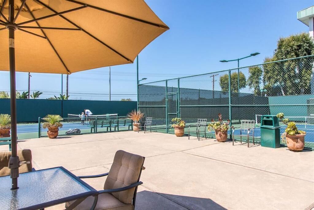 En udendørs tennisbane med net, plantekasser og et bord med parasol.