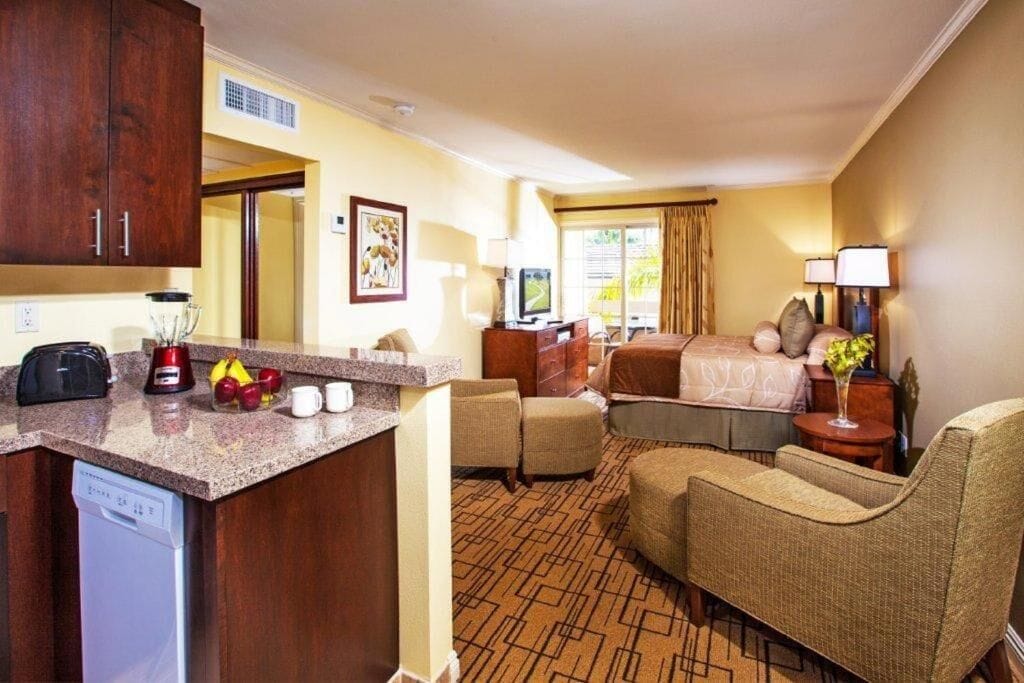 A hotel room with a kitchenette, a bed, a seating area, and a television.