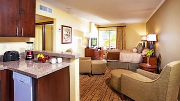 A hotel room with a kitchenette, a bed, a seating area, and a television.