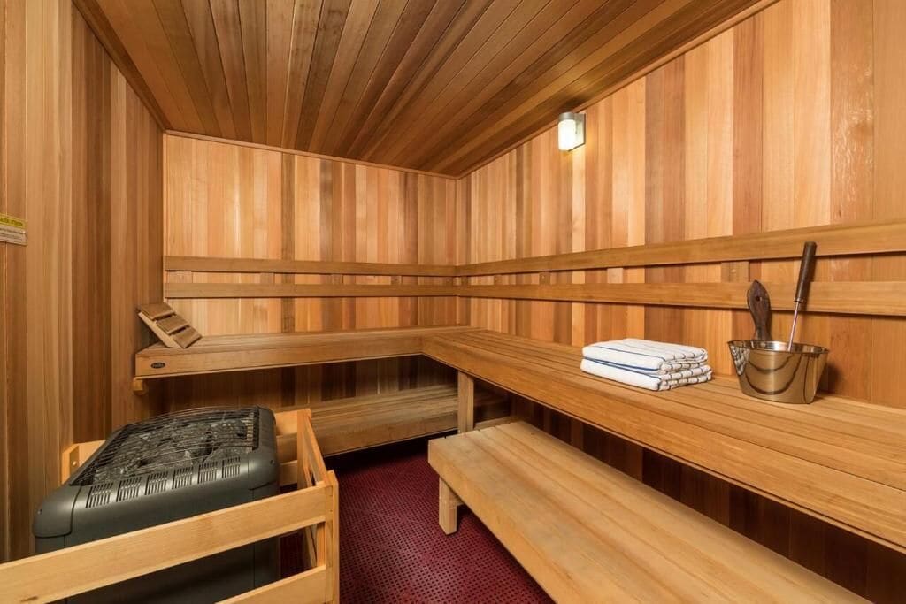A sauna with wooden benches and a bench seat, a metal bucket, and a towel stack.