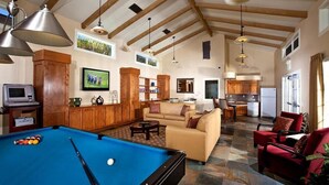 A spacious living area with a pool table, a sofa, and a red armchair. There is a kitchen in the background with a dining table and chairs. - Winners Circle Solana Beach Del Mar Resort (Solana Beach)