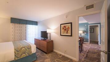 A hotel room with a bed, a desk, a chair, a television, a lamp, and a painting on the wall.