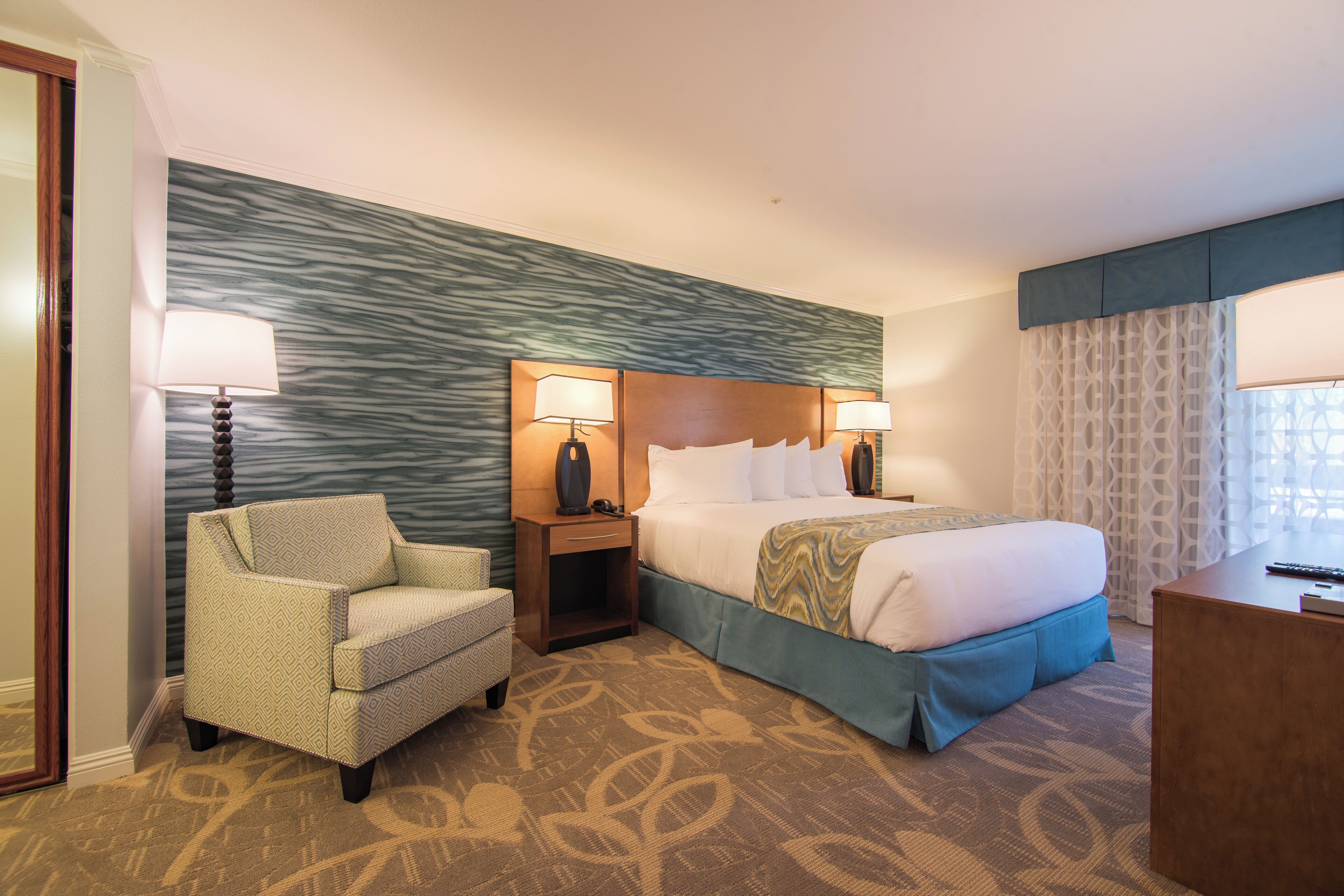 A hotel room with a bed, two bedside lamps, a chair, a nightstand, and a desk.