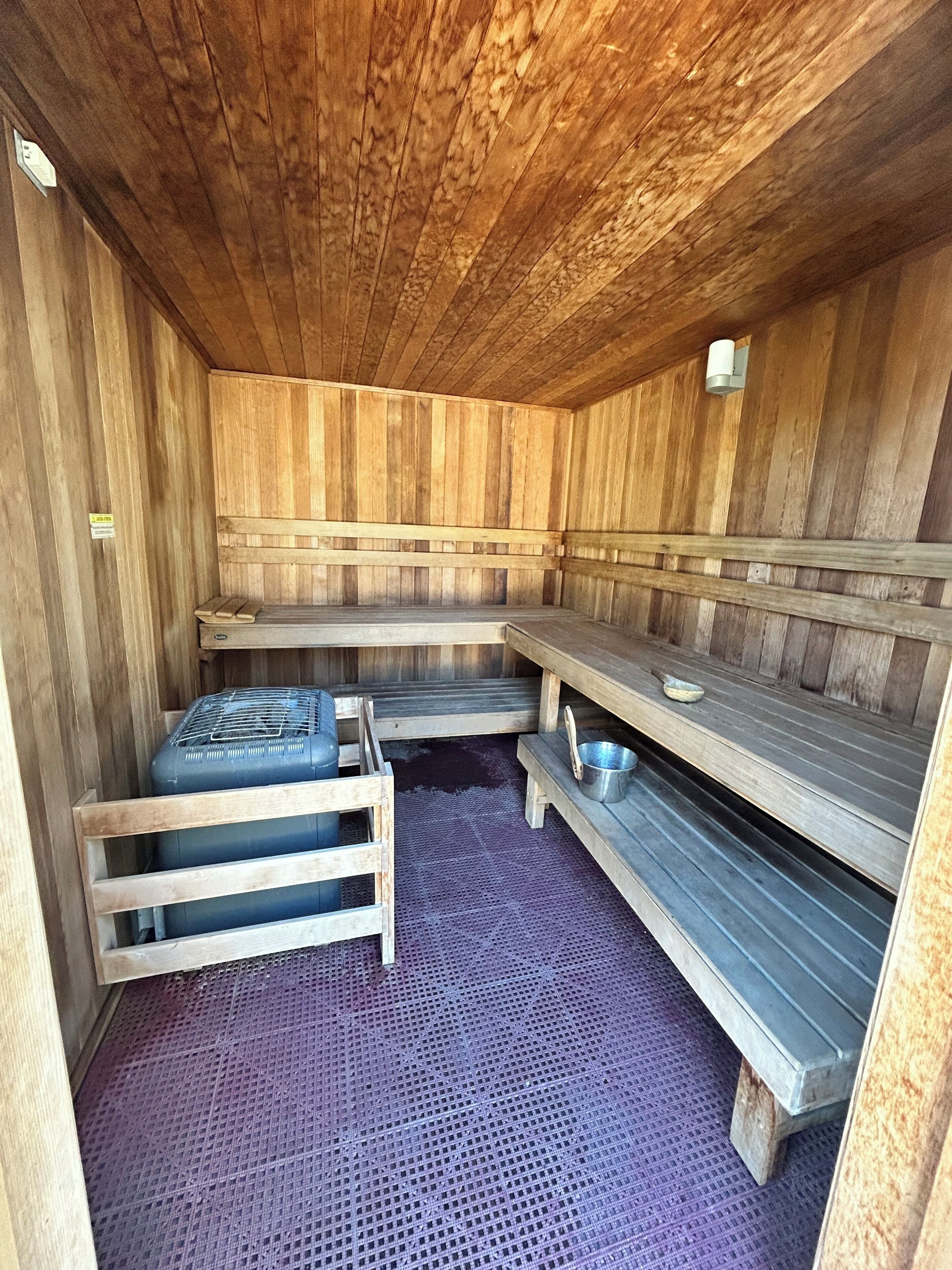 A sauna with wooden walls and benches, a small shelf with a bowl, and a mat on the floor.