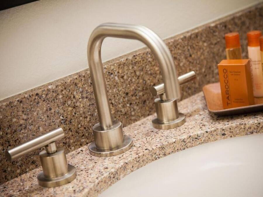 A bathroom with a granite countertop, a silver faucet, and a tray with three bottles of toiletries.