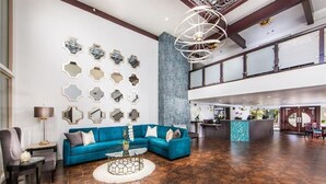 A spacious lobby with a blue sofa, a round coffee table, and a decorative wall with hexagonal mirrors. - Winners Circle Solana Beach Del Mar Resort (Solana Beach)