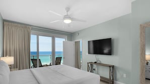 Una camera d'albergo con un letto, una ventola a soffitto, una TV, un comodino e vista sull'oceano.