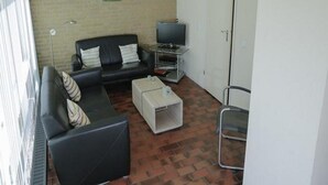 A living room with a black sofa, a white coffee table, a television on a stand, and a clock on the wall.