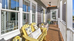 Une véranda avec des fauteuils Adirondack jaunes, une petite table ornée d’un vase de fleurs et une vue sur l’intérieur de la maison à travers de grandes fenêtres.