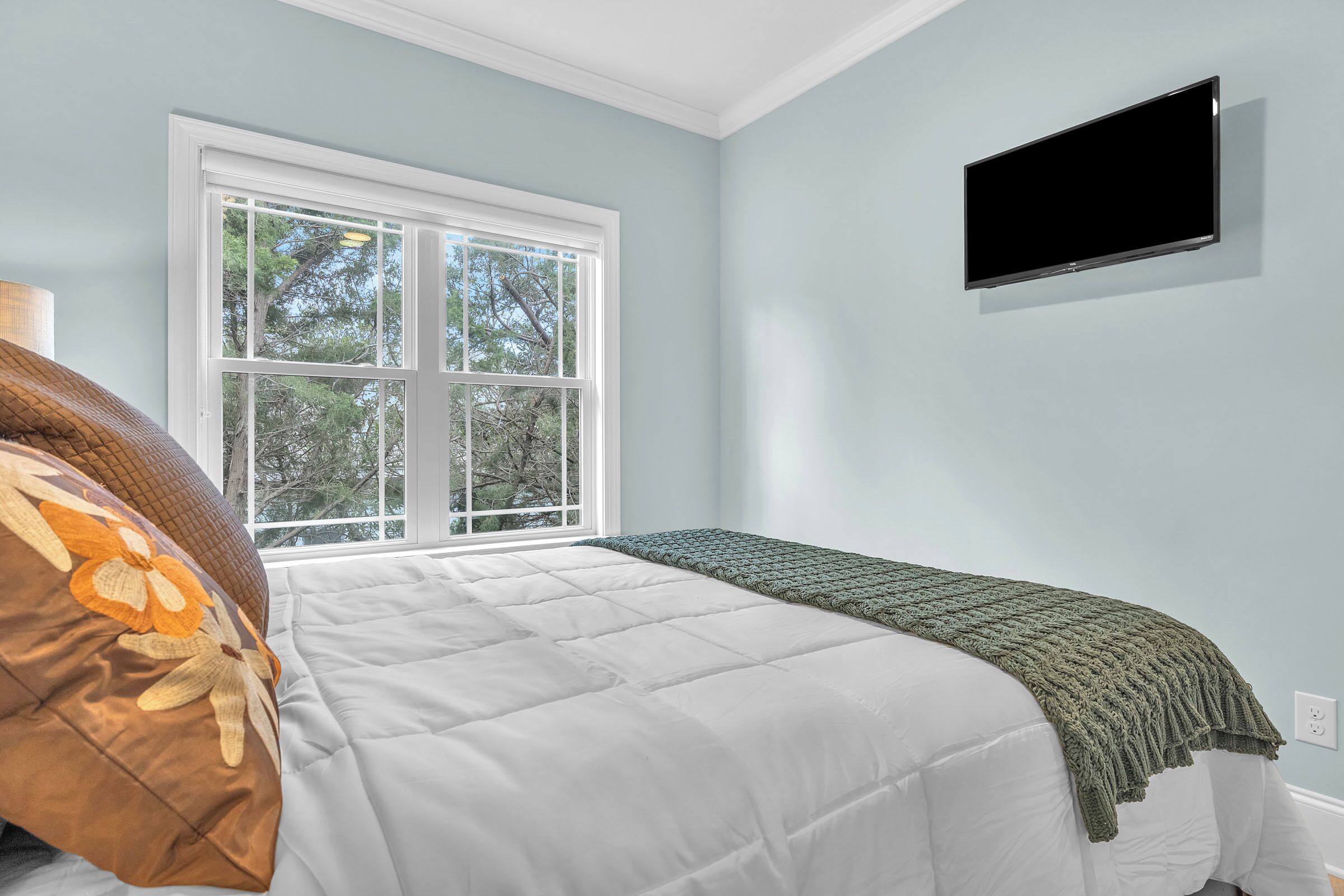 A bedroom with a bed, a window, and a TV mounted on the wall.