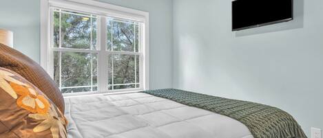 A bedroom with a bed, a window, and a TV mounted on the wall.