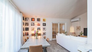 Ein modernes Wohnzimmer mit Essbereich, ausgestattet mit einem großen Esstisch, bequemen Sitzgelegenheiten und einem weißen Sofa.