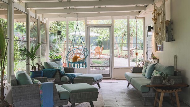 Ein sonnendurchfluteter Raum mit Korbmöbeln, großen Fenstern und Blick auf den Garten.
