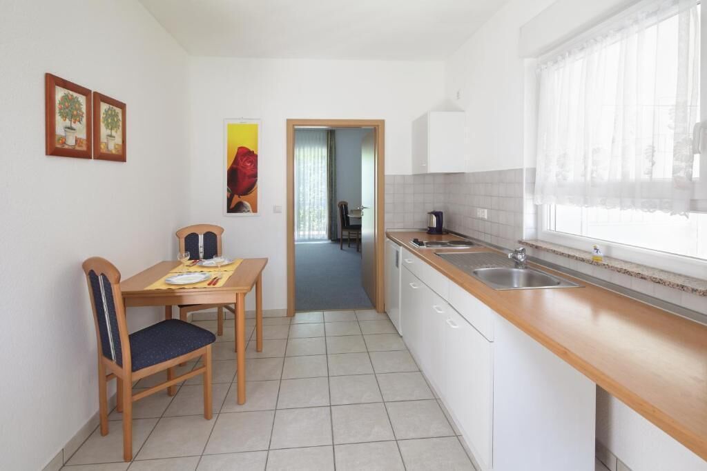 A compact kitchen with a dining area, a view through a doorway, and a window with sheer curtains.