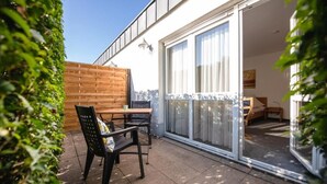 A patio with a wooden table and chairs, a wooden fence, and a sliding glass door leading to an interior space. - Hotel Phönix garni (Rastatt)