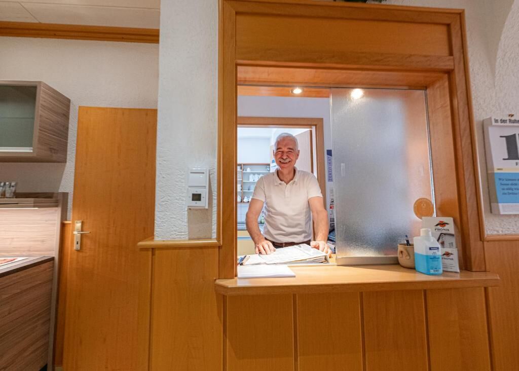 A reception desk with a wooden frame, a mirror, and a counter with a bottle of hand sanitizer and a brochure.