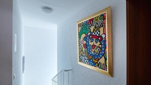 A hallway with a colorful abstract painting on the wall, a white door, and a white railing. - Hotel Phönix garni (Rastatt)