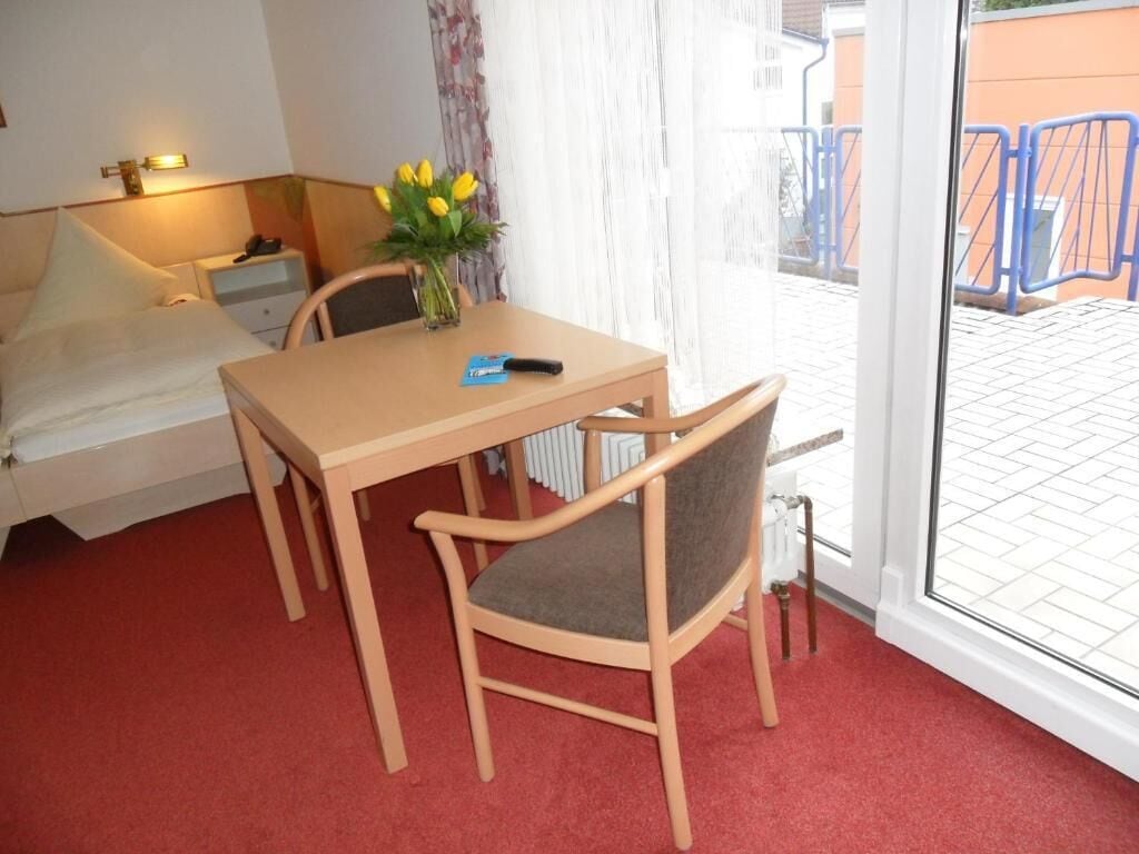 Une chambre d’hôtel avec un lit, une table et une chaise, un vase avec des fleurs et une vue sur l’extérieur.