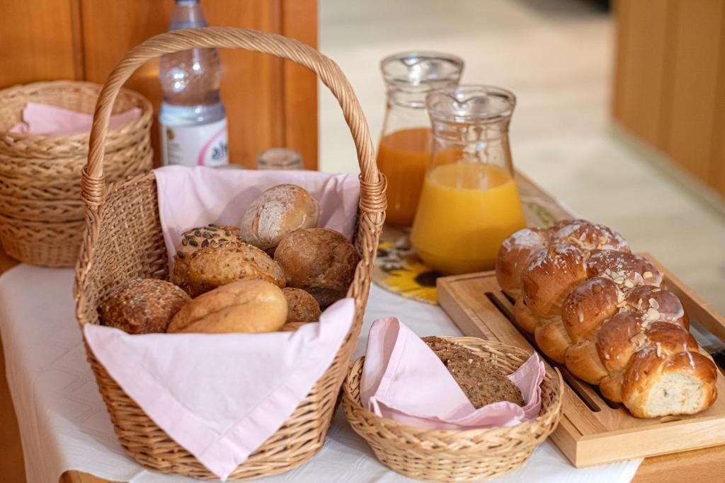 A breakfast table with baskets of bread, a loaf of challah bread, and a pitcher of orange juice.