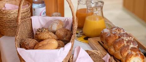 A breakfast table with baskets of bread, a loaf of challah bread, and a pitcher of orange juice.