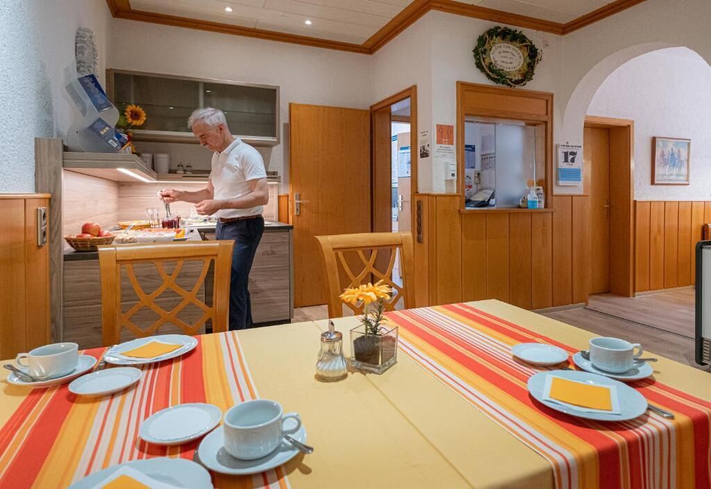 A dining area with a table set for four, a man preparing food, and a kitchen in the background.
