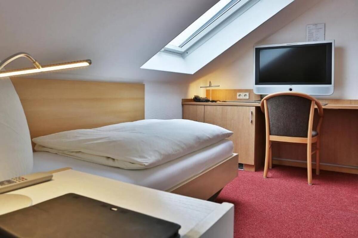 A hotel room with a bed, a desk with a computer, a chair, a TV, and a skylight.