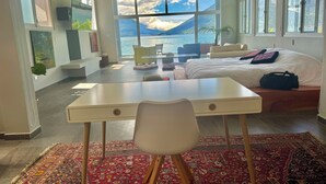 A modern hotel room with a large bed, a desk, and a view of the sea.