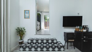 Un salon moderne doté d’un téléviseur à écran plat, d’un petit coin cuisine avec un réfrigérateur et un four à micro-ondes, d’une plante en pot et d’un tapis à motifs.