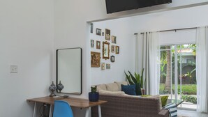 Une pièce avec un bureau en bois, une chaise bleue, un canapé en osier et un grand miroir.