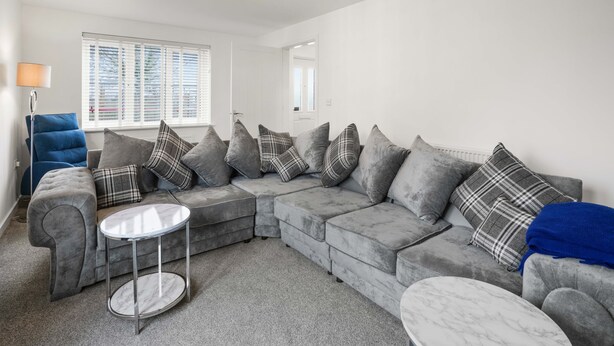 A modern living room with a grey sectional sofa, a round coffee table, and a blue armchair. - Broads Escape/ - 3 Bedroom House in Oulton Broads (Lowestoft)