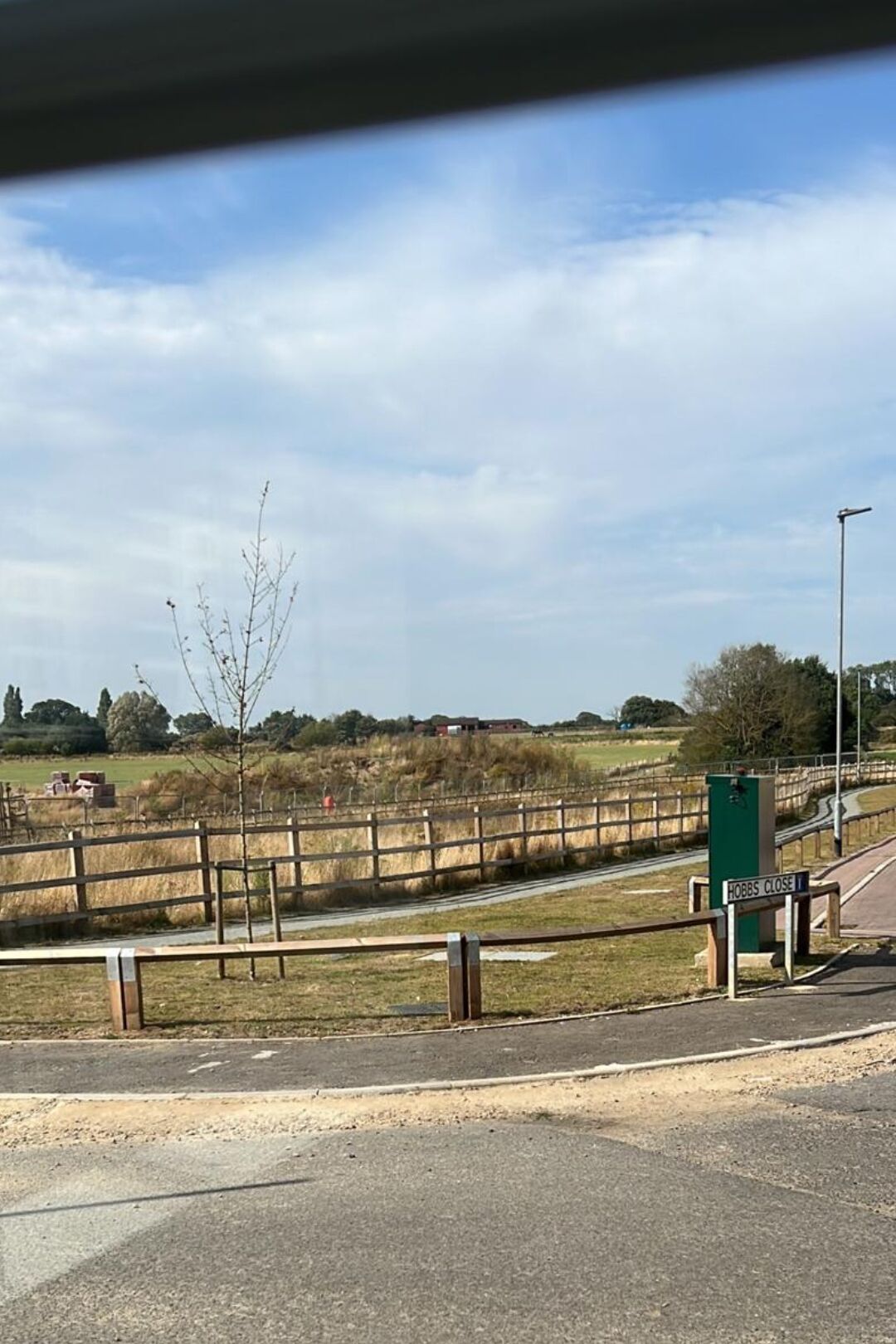 A rural landscape with a fence, a road, and a sign indicating 'HOBBS CLOSE'.