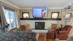 Una sala de estar con un televisor de pantalla plana grande montado en la pared, una chimenea y diversas opciones de asientos, incluyendo un sofá, sillas y un sillón.